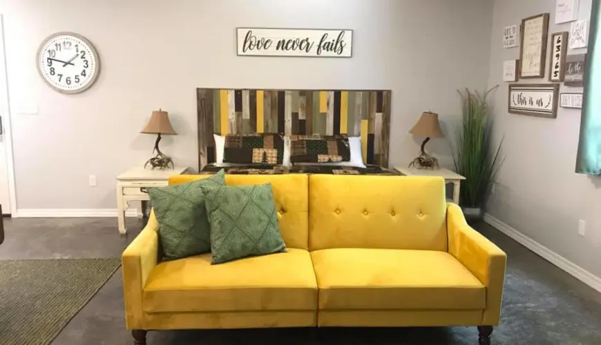 A yellow couch with two pillows on top of it.