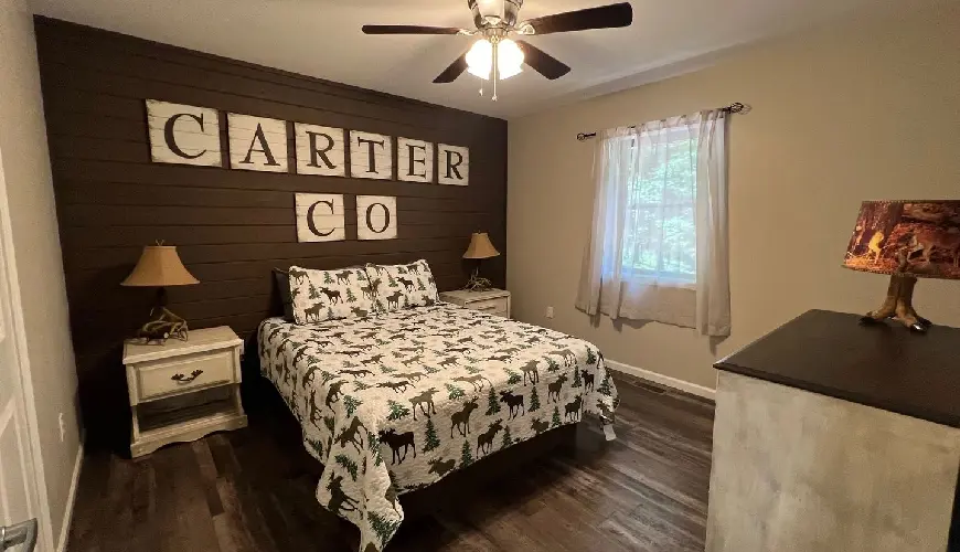 A bedroom with a bed, ceiling fan and wooden floors.