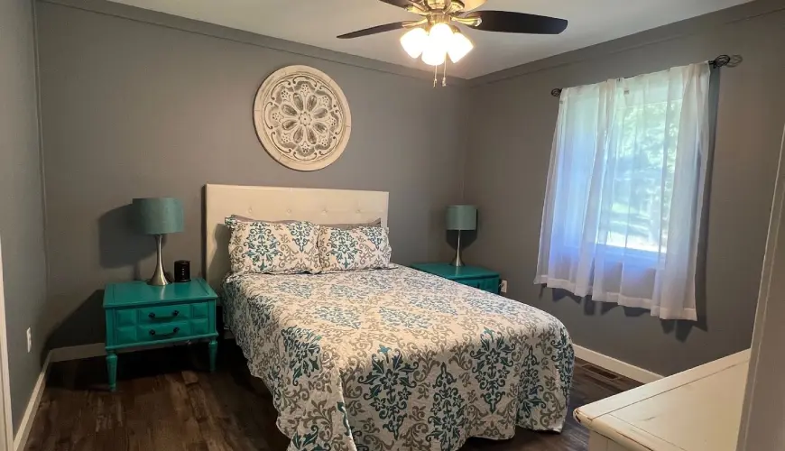 A bedroom with a bed, two night stands and a ceiling fan.