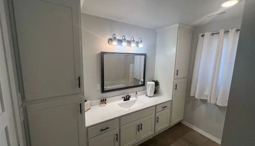 A bathroom with white cabinets and a mirror.